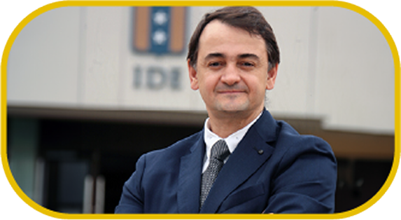 Professional man in a navy suit smiling, standing outdoors in front of a modern building.