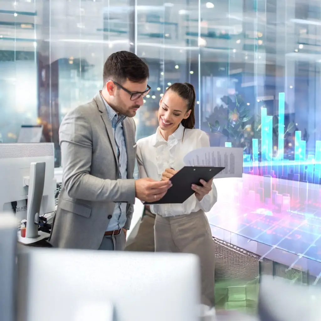 Two professionals review a clipboard together in a modern office, with holographic data visuals in the background